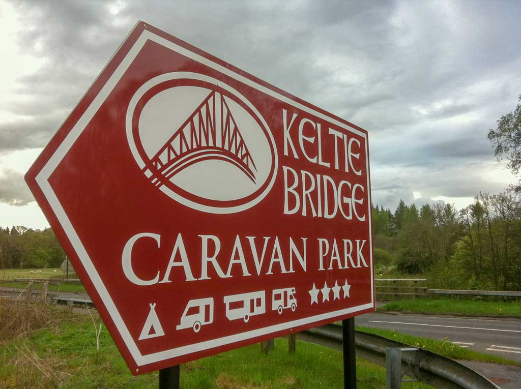 purple red and white arrow shape road sign sign directing traffic to a Keltie Bridge Caravan Park in Callander Scotland